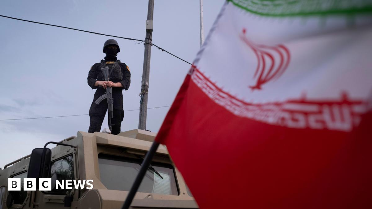 An armed Iranian police officer stands guard on an armored vehicle, monitoring the area during a state-run religious rally in downtown Tehran, Iran, on April 29, 2026. An Iranian flag is seen in the foreground.