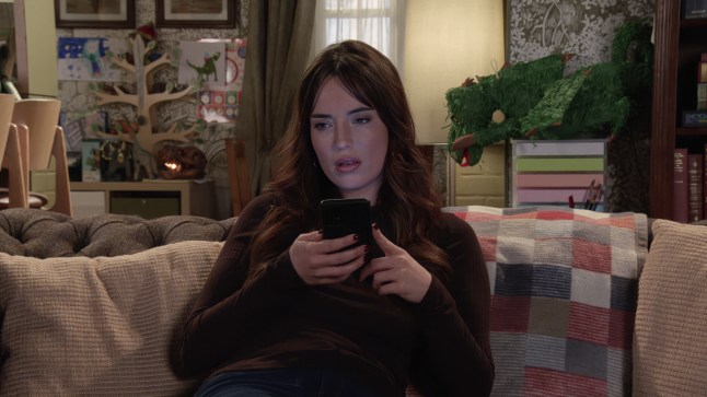 Jodie sits messaging on her phone in Corrie