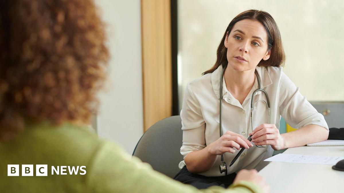 A GP wearing a stethoscope around her neck talks to a patient.