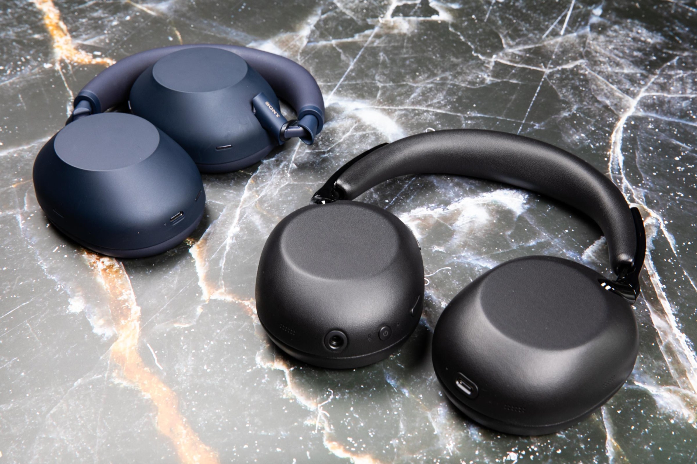 The Sony 1000X The Collexion headphones in black next to the WH-1000XM6 headphones in blue on a marble surface.