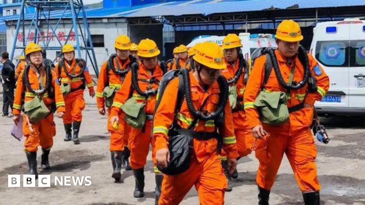 Rescuers in orange safety suits and helmets walking near industrial buildings