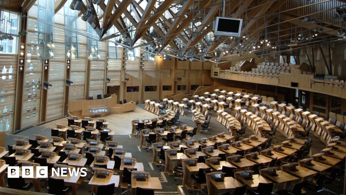An empty Holyrood chamber - several rows of pine desks are arranged in a semi-circle facing the presiding officer's lectern at the front, while soft light streams in from above.