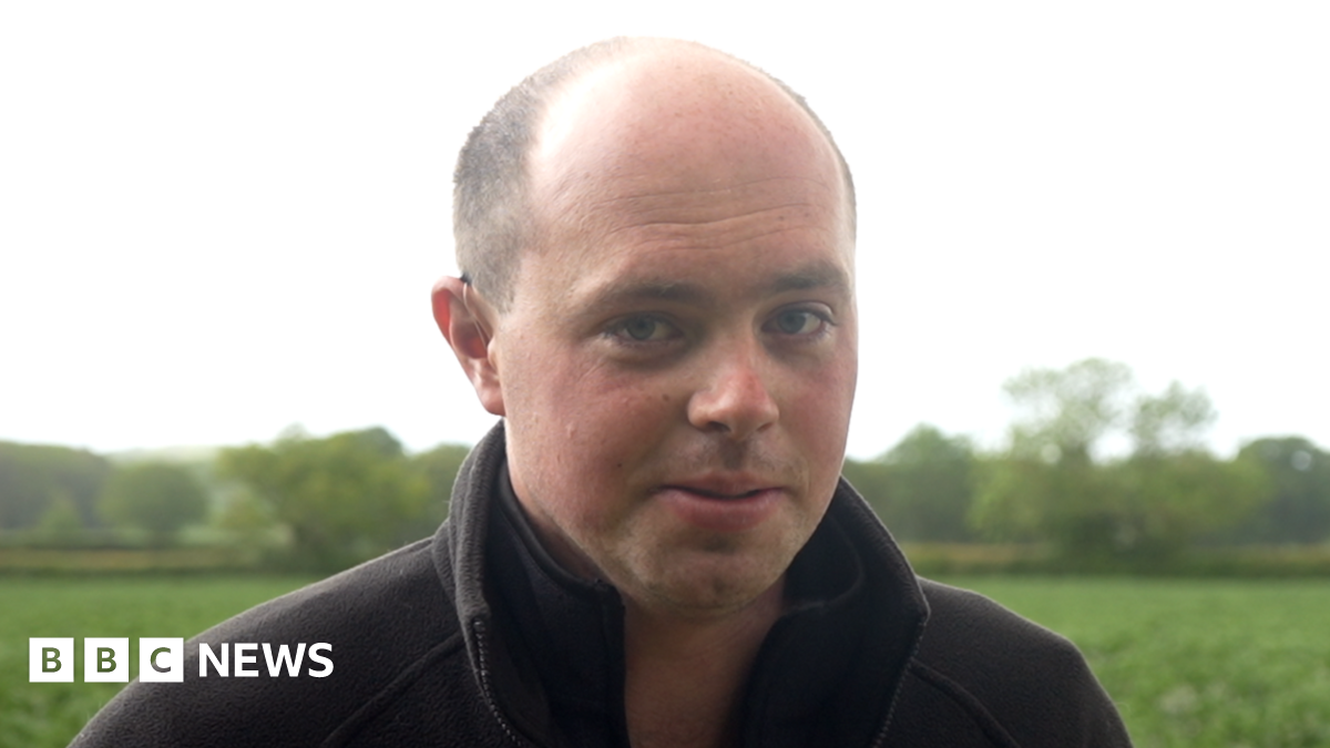 Matthew Register has a shaved head and is wearing a black jumper in front of a green field.