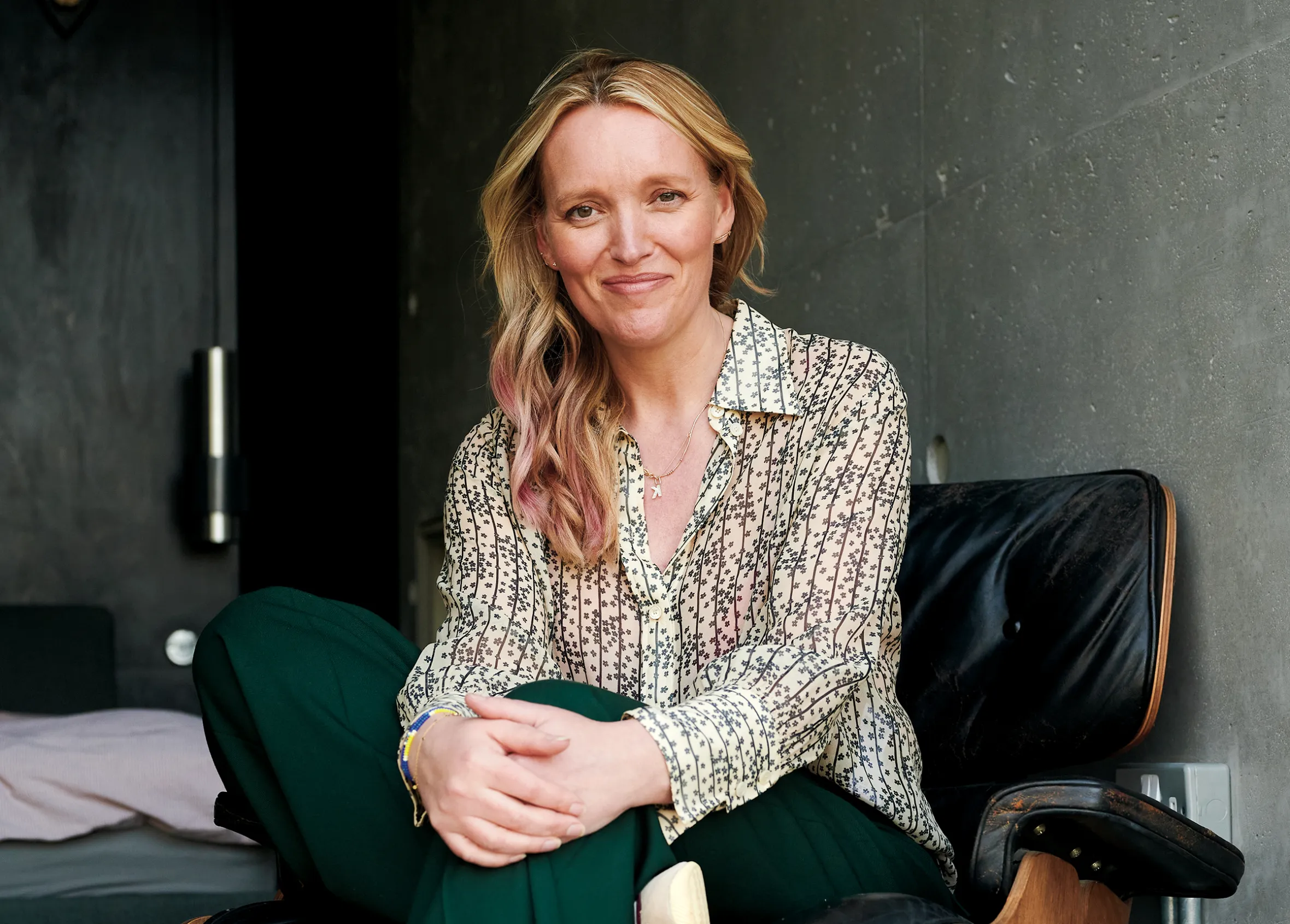 Kate Prince, founder of Ancient + Brave, smiles while sitting in a black leather and wood chair.