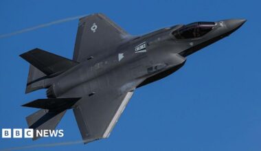 A black F-35 Lightning II stealth fighter jet turns through a clear blue sky.