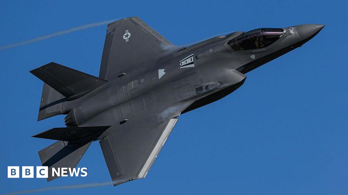 A black F-35 Lightning II stealth fighter jet turns through a clear blue sky.