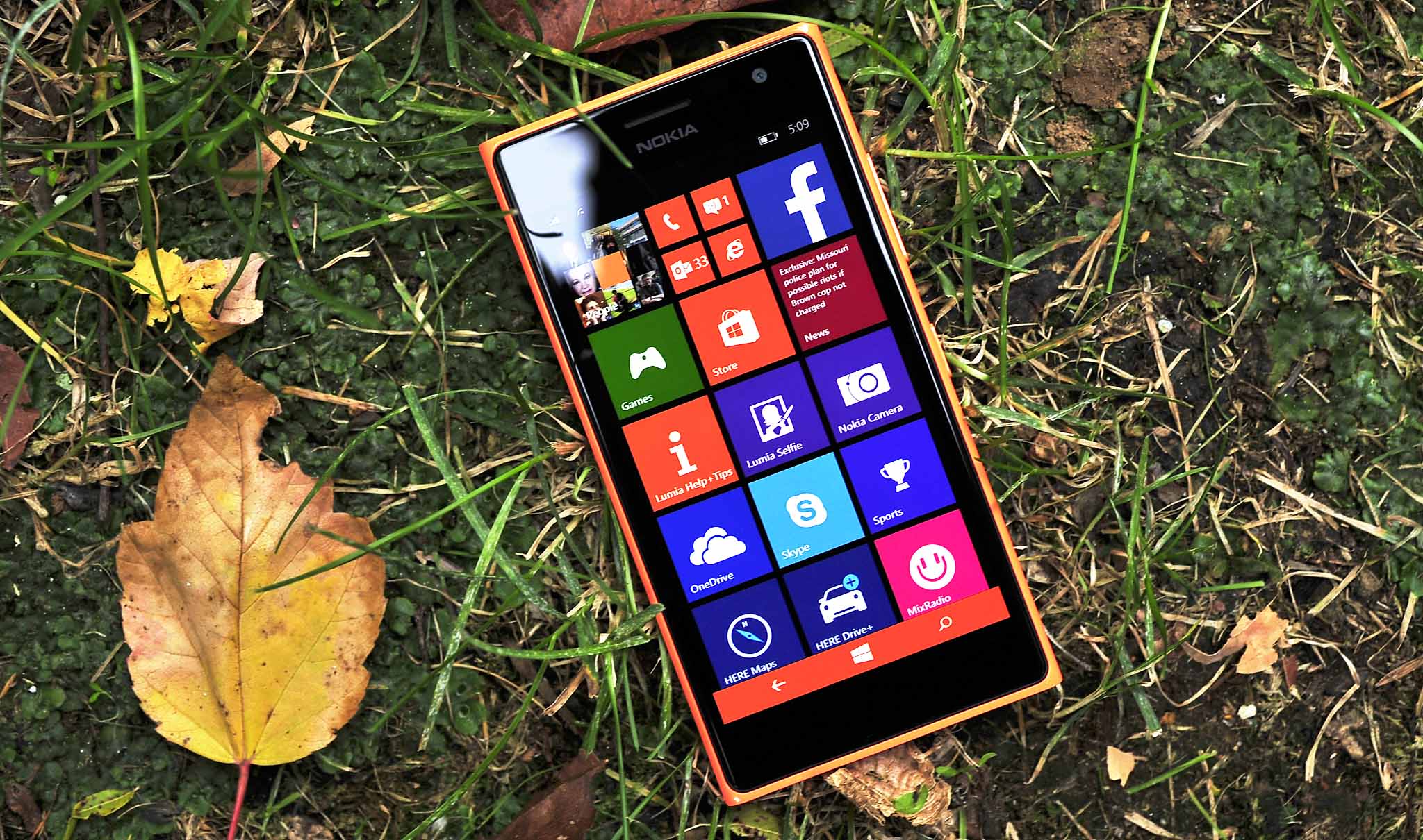 Nokia Lumia 735 in orange on grass with autumn leaves