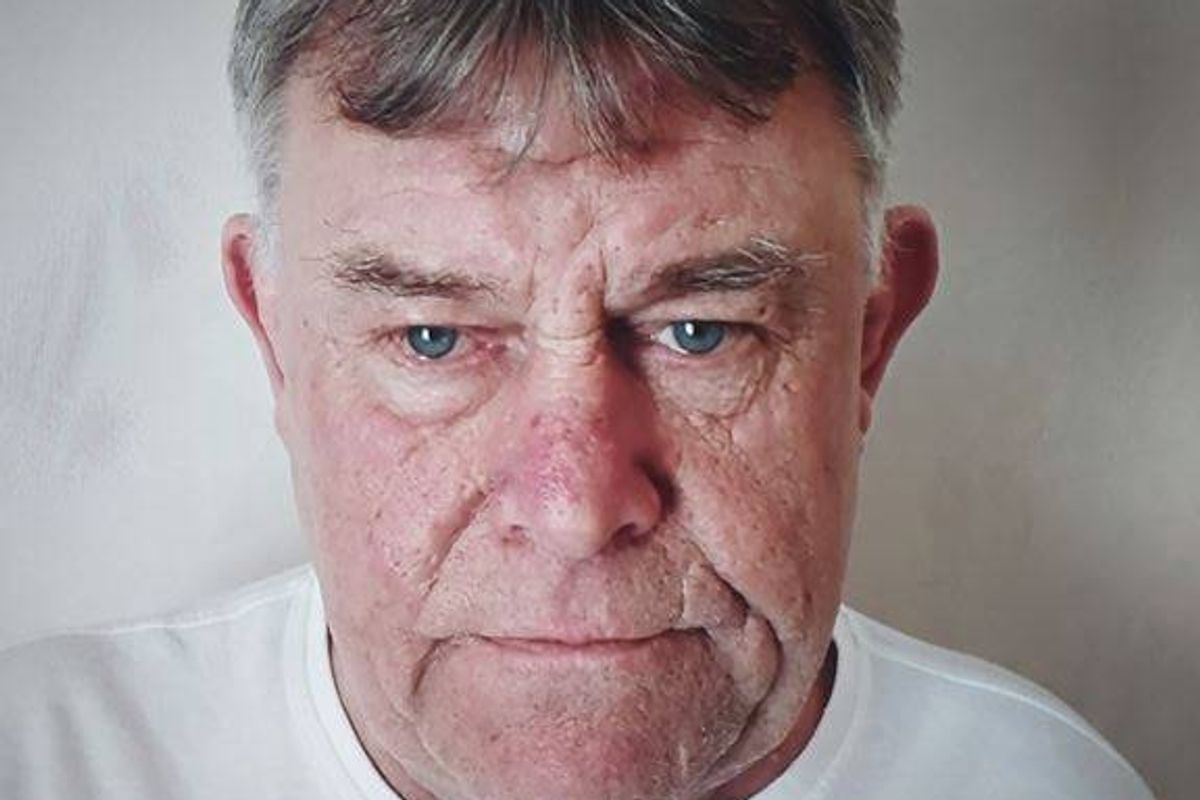A white man in his 60s with dark grey hair and blue eyes