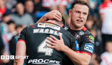 Wigan Warriors player Jai Field smiles and embraces team-mate Jake Wardle after Wardle had scored a try, both players kitted out in black.