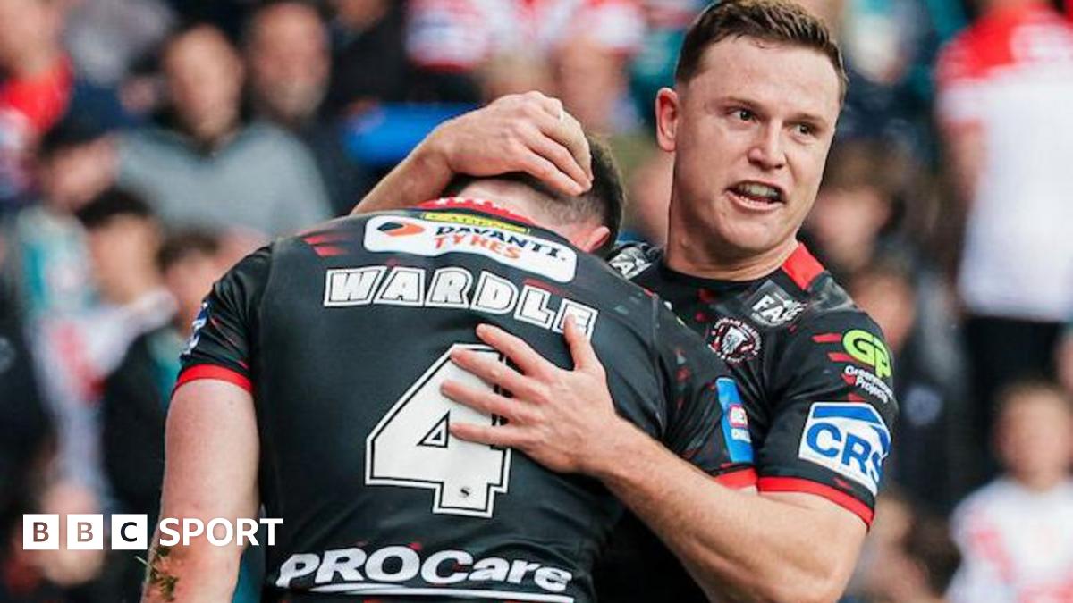Wigan Warriors player Jai Field smiles and embraces team-mate Jake Wardle after Wardle had scored a try, both players kitted out in black.