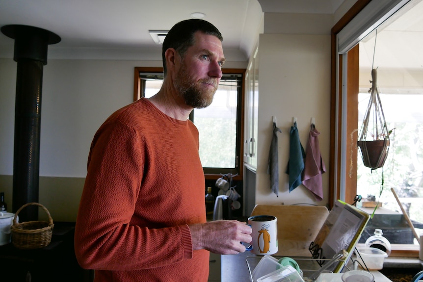 A man holding a coffee mug in a kitchen.