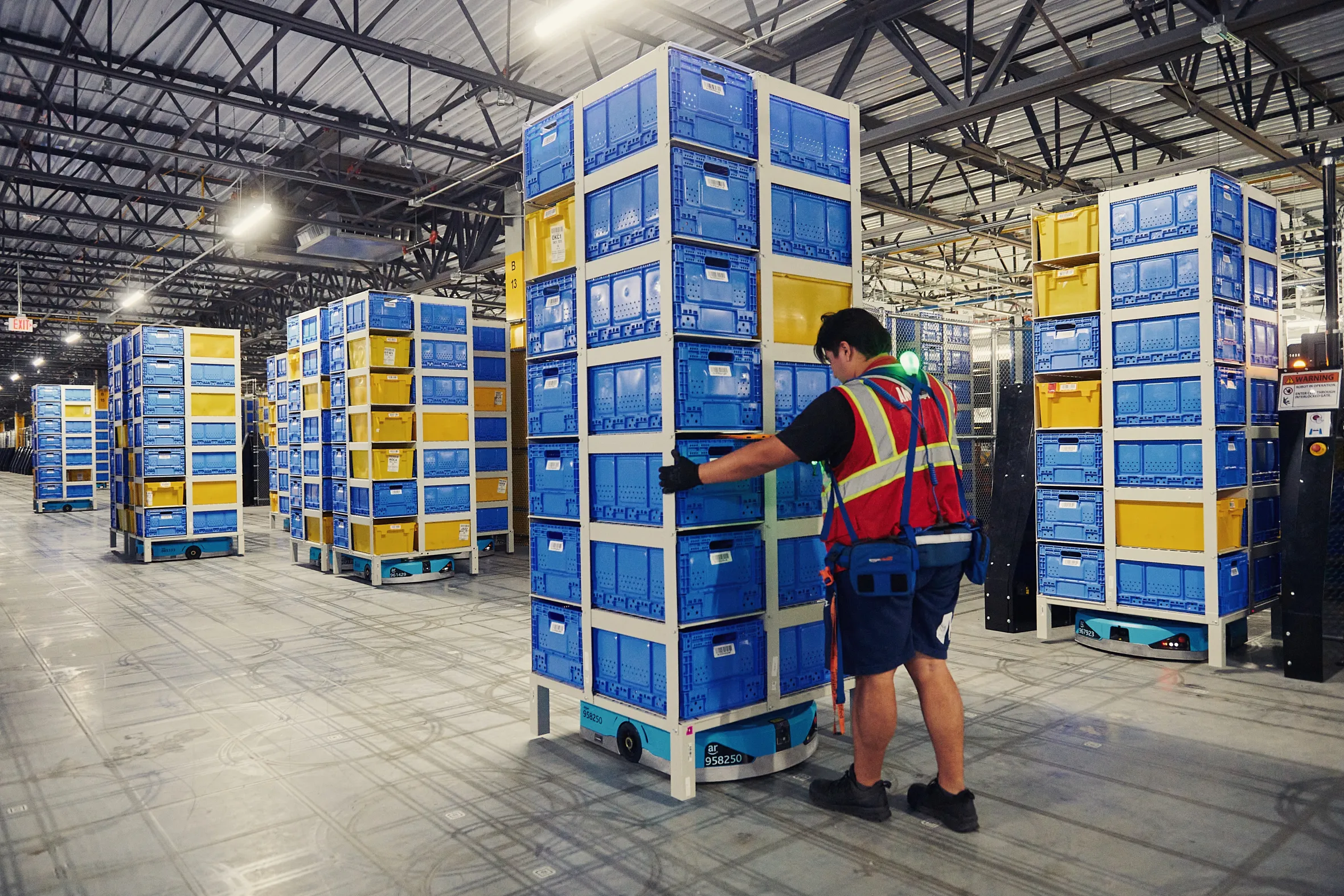 An Amazon employee loads a tote onto a mobile robotic unit in a warehouse.