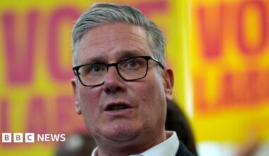 Sir Keir Starmer pictured wearing a dark suit with Labour placards in the background