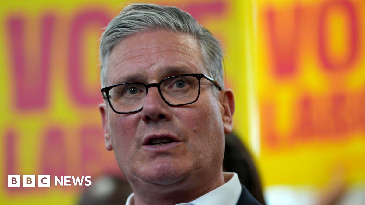 Sir Keir Starmer pictured wearing a dark suit with Labour placards in the background