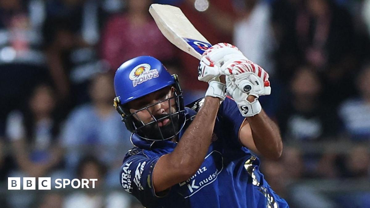 Rohit Sharma, wearing a blue shirt, blue helmet, and white batting gloves with red markings, holds his bat over his left shoulder after playing a shot