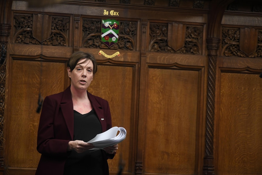 A woman wearing a maroon suit jacket speaking in the British House of Commons.