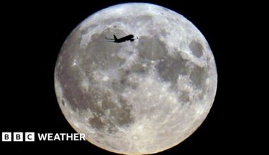 An aeroplane silhouetted across a bright full Moon in the night sky