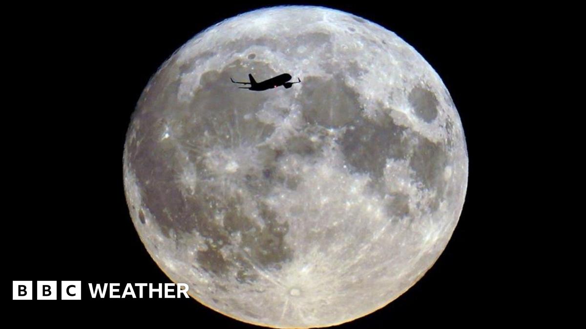An aeroplane silhouetted across a bright full Moon in the night sky