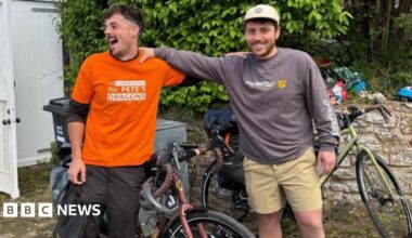 Conrad (left) and Bobby with their hands on each others shoulders. They have biked behind them. They are both smiling.