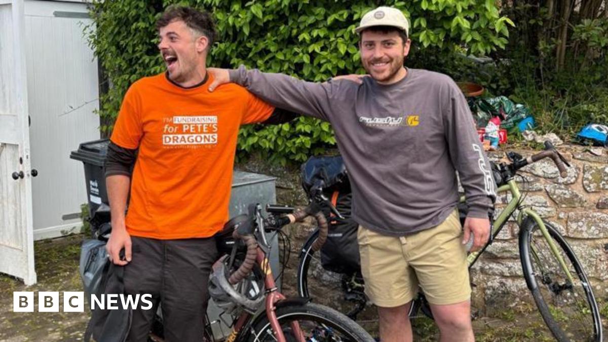 Conrad (left) and Bobby with their hands on each others shoulders. They have biked behind them. They are both smiling.