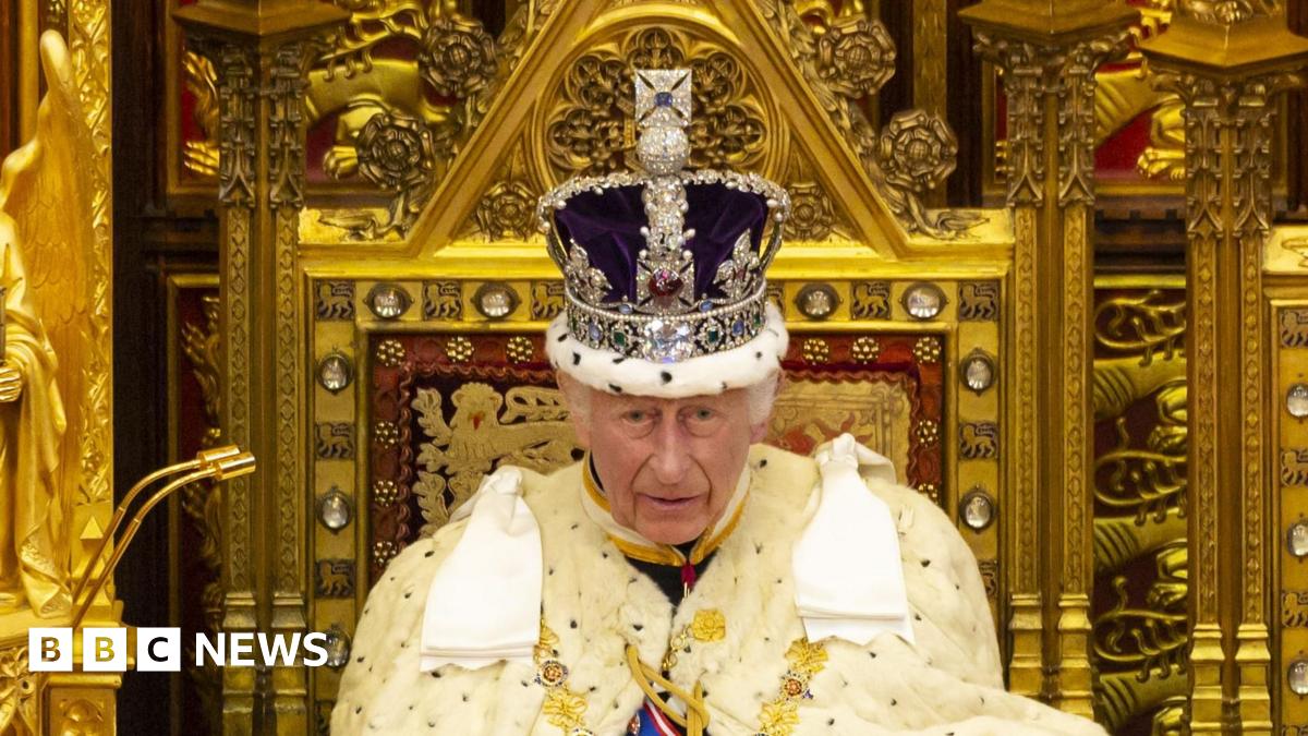 King Charles wearing a crown and sitting on a gold throne in white ermine robes