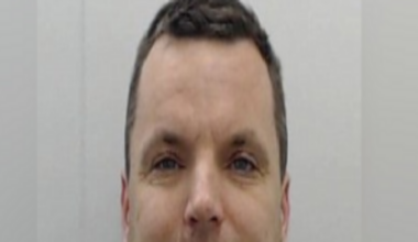 Man smiles at camera in mugshot.
