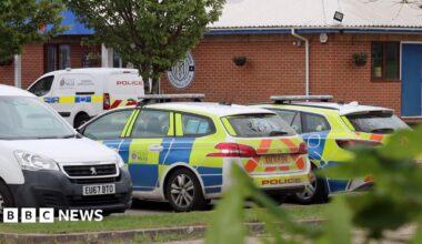 Police cars and vans parked outside Maldon and Tiptree FC's brick clubhouse.