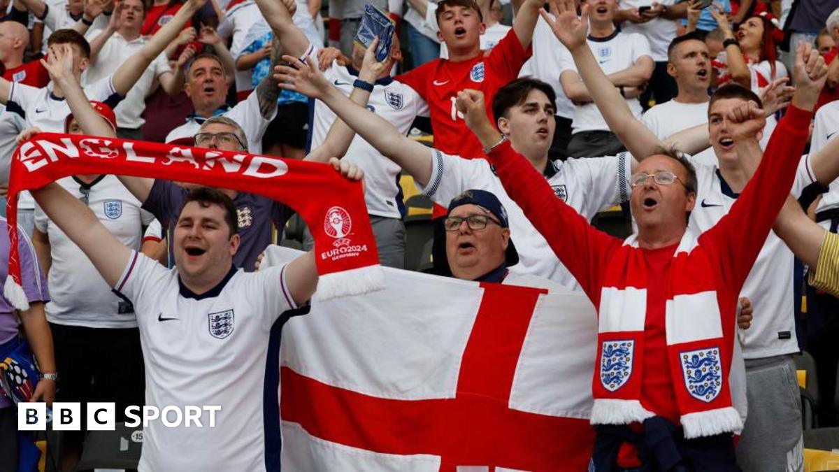 England fans before the Euro 2024 final, many wearing white team shirts, while some have scarves and one holds a red and white Cross of St George flag