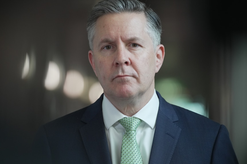 man in blue suit and green tie with still face looking straight ahead