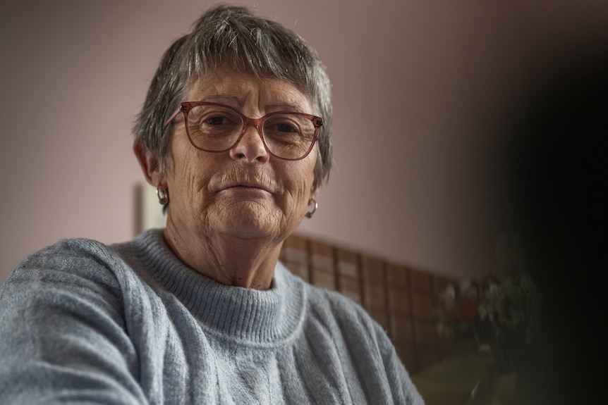 An older woman with glasses looks into the camera