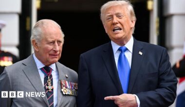 King Charles standing next to US President Donald Trump. who is speaking and pointing towards the monarch.