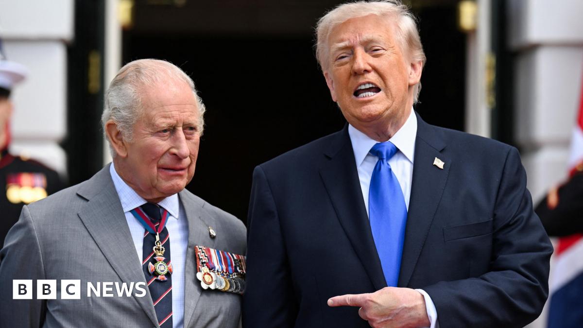 King Charles standing next to US President Donald Trump. who is speaking and pointing towards the monarch.