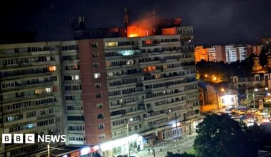 A small fire is seen on top of a multi-storey building at night