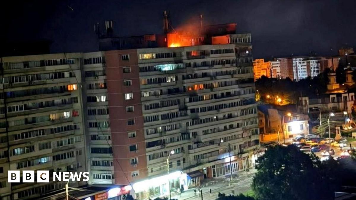 A small fire is seen on top of a multi-storey building at night
