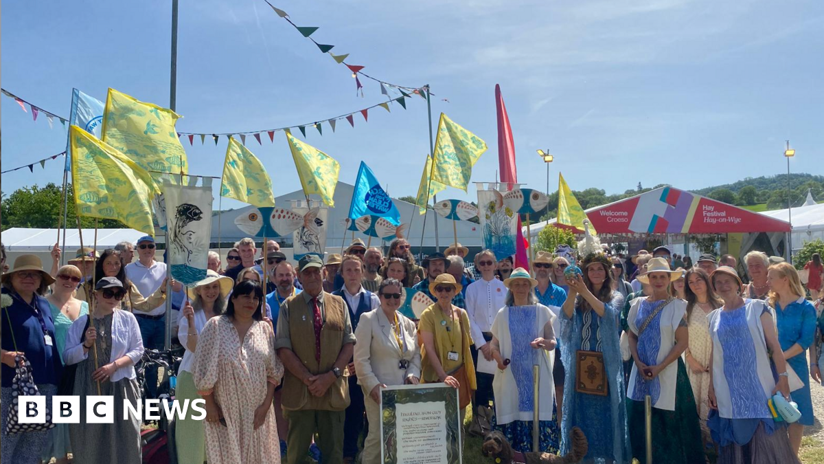 A large group of people, some dressed in river costumes, stand outside the Hay Festival entrance