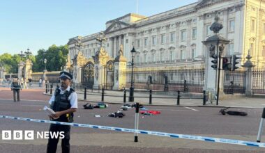 Remnants of an e-scooter crash outside Buckingham Palace with police tape and officers seen in the foreground.
