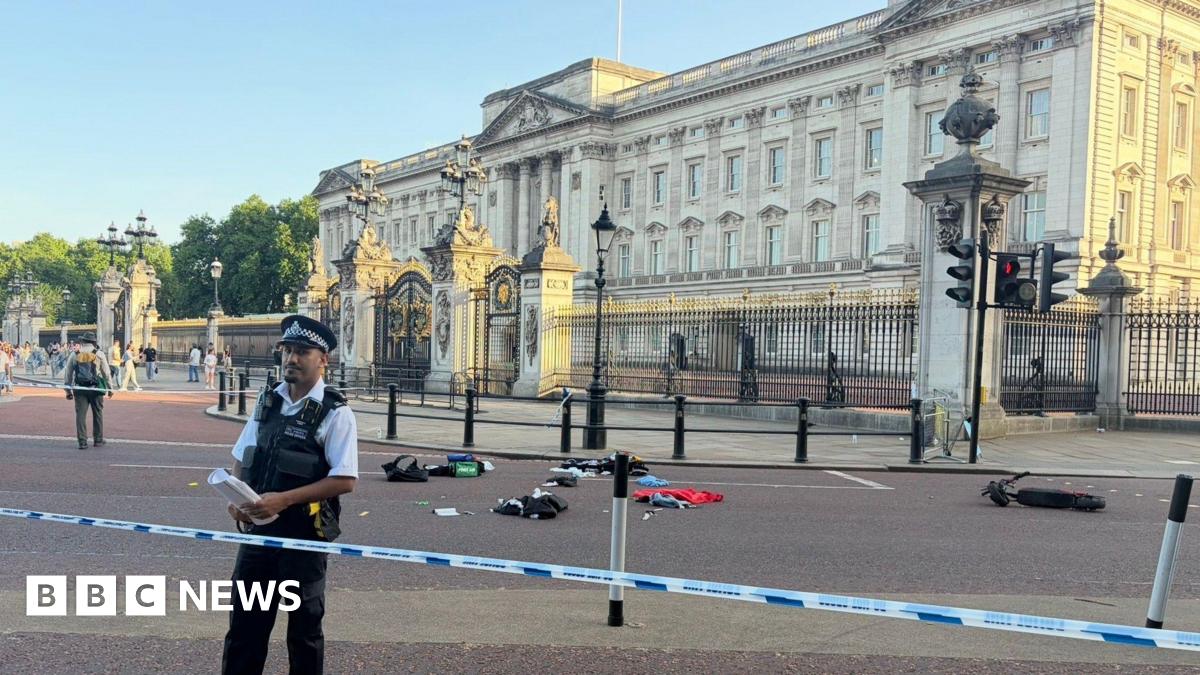 Remnants of an e-scooter crash outside Buckingham Palace with police tape and officers seen in the foreground.