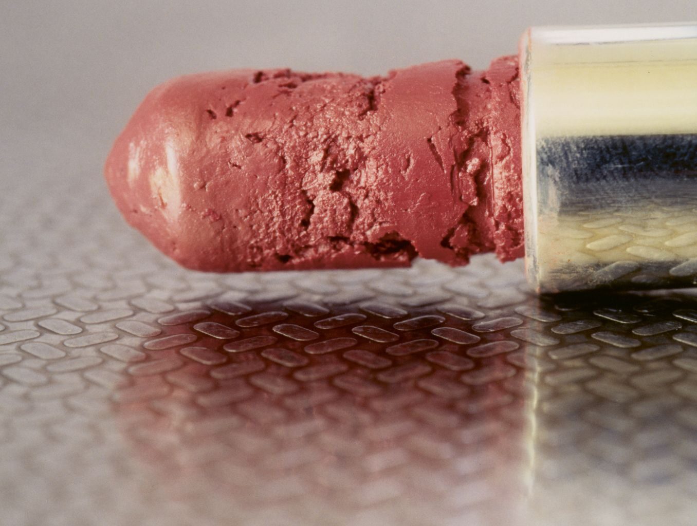Detailed photograph of a pink lipstick on textured surface with visible cracks and wear indicating age and use.