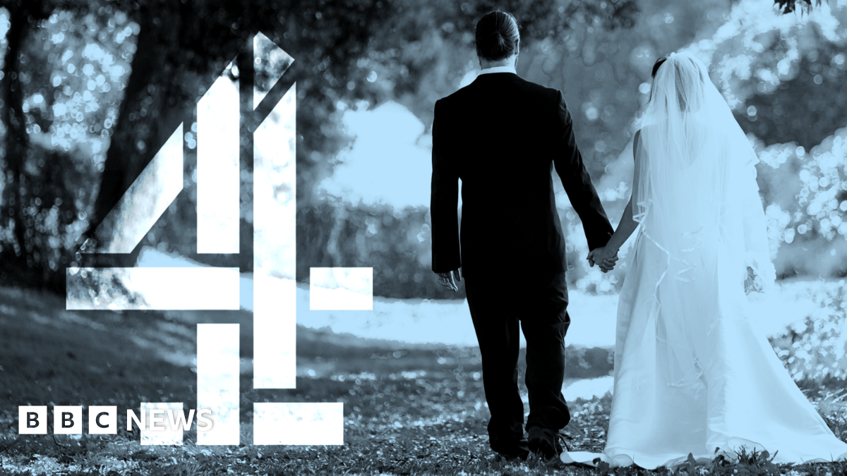 Black-and-white image of two people in formal wedding attire walking away from the camera while holding hands along a tree-lined outdoor path. One person wears a long veil and flowing dress, and the other wears a dark suit. On the left side of the image, a large stylised Channel 4 logo appears, partially overlaid on the scene.