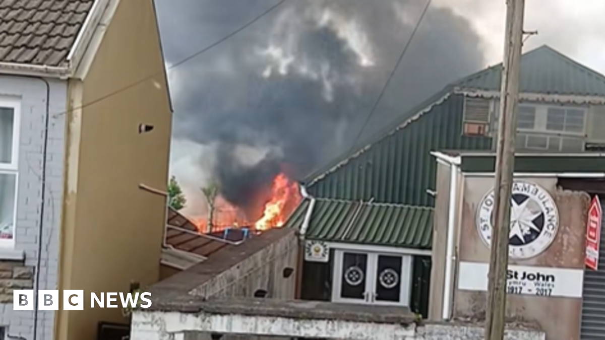 A large fire behind a house and a Welsh Ambulance building. A cloud of black smoke rises in the air.