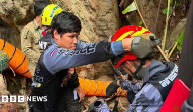 Four rescuers wearing helmets stand at the entrance to a cave