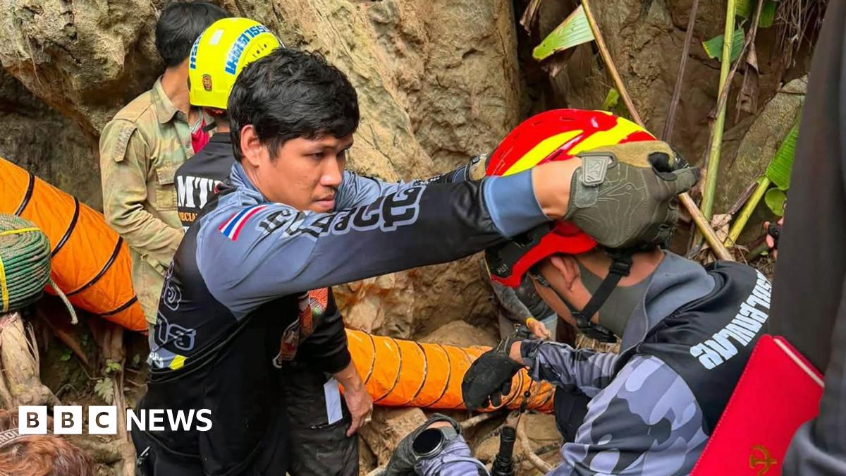Four rescuers wearing helmets stand at the entrance to a cave