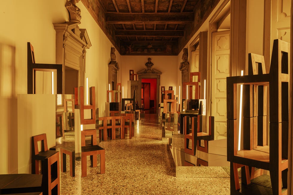 A corridor featuring unique wooden chairs and reflective surfaces.
