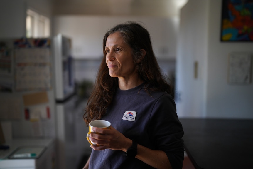 A woman standing in a kitchen holding a coffee mug.