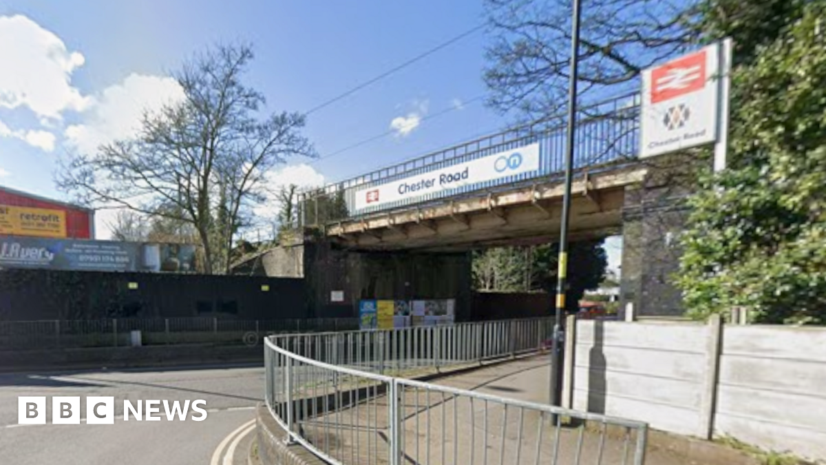 A road with metal railings in the foreground and a bridge overhead with the words Chester Road on it