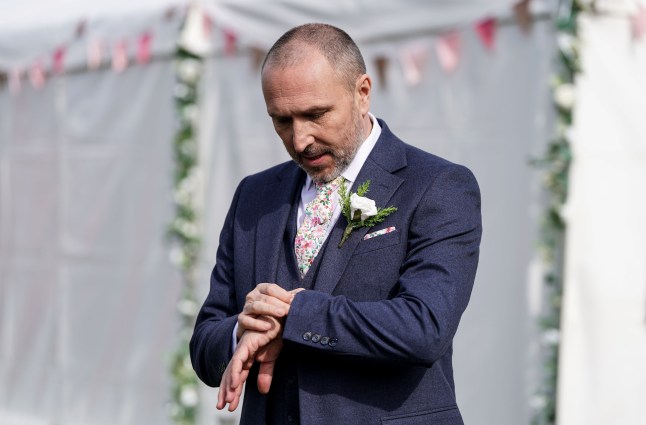 Ross standing at his wedding looking at his watch in EastEnders