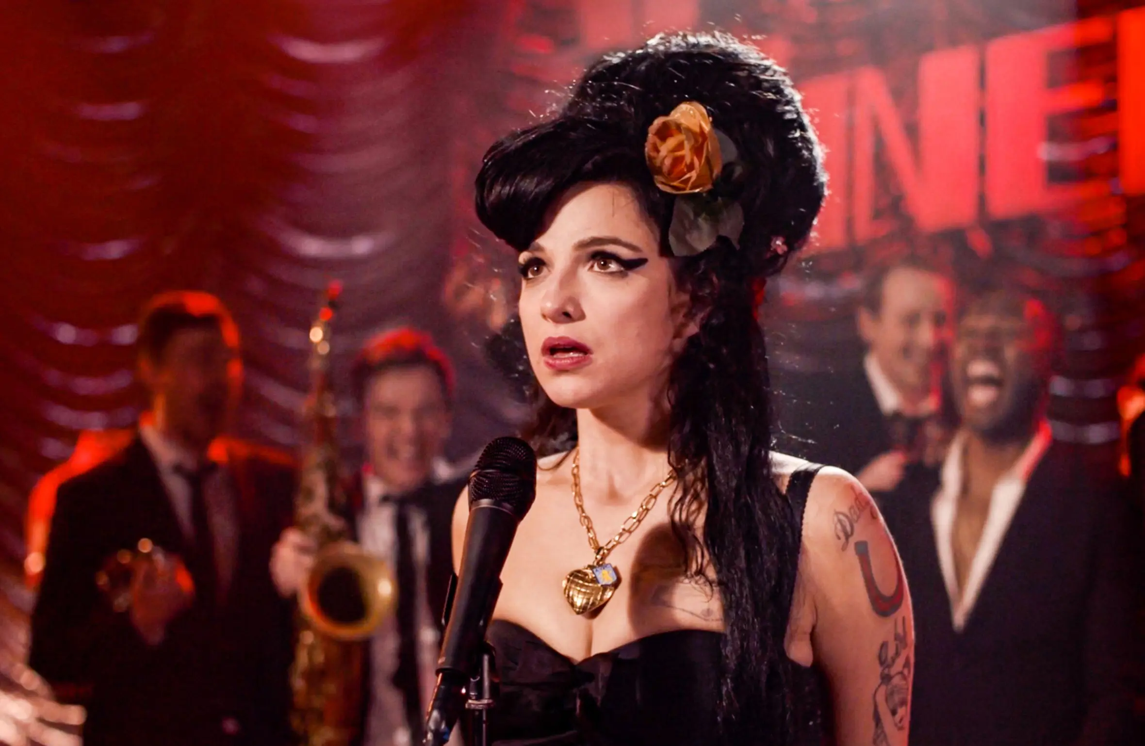 Marisa Abela as Amy Winehouse, performing on stage with a band in the film "Back to Black."