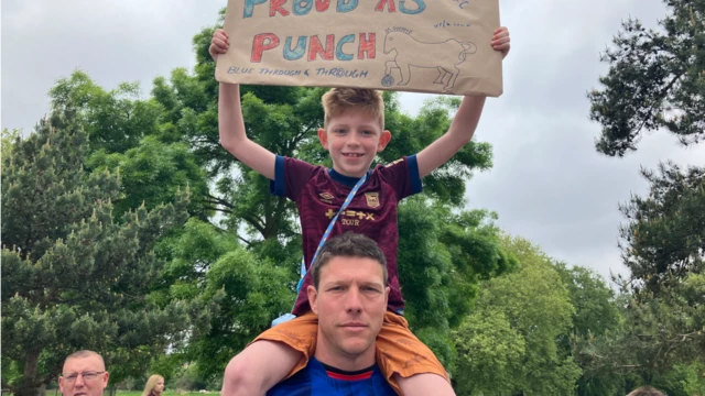 Simon and his son Lochland, who is on his shoulders holding a 'Proud As Punch' sign.