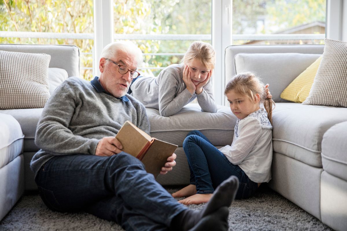 A grandparent is reading a book to two younger children.