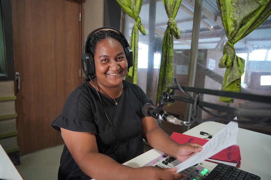 Stella at work holding papers with headphones on at the Tuvalu Broadcasting Corporation.
